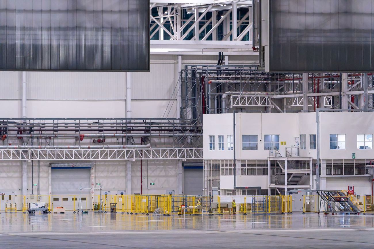 Large, clean modern factory interior with overhead piping, a control office and yellow safety barriers on the floor